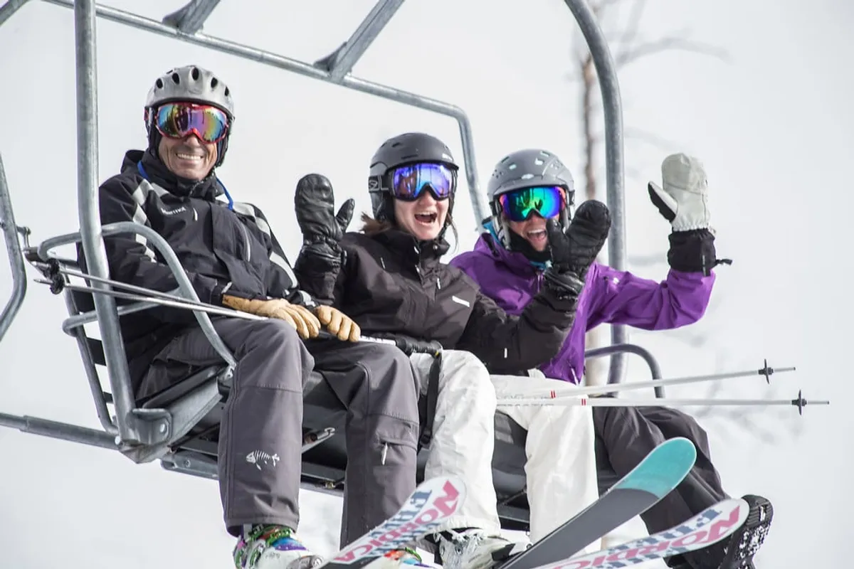 People ride a ski lift over a snowy landscape, their ski gear and joyful expressions capturing the excitement of a day on the mountain. The backdrop features snow-laden trees and slopes, inviting thoughts of thrilling ski runs.