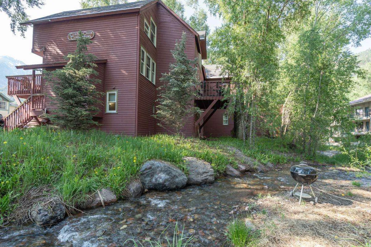 This image features the property’s inviting wooden exterior set beside a sparkling stream. A grill and outdoor seating area are arranged in a garden-like space. Lush greenery and the sound of moving water create a relaxing natural ambiance, ideal for unwinding after a day exploring town.