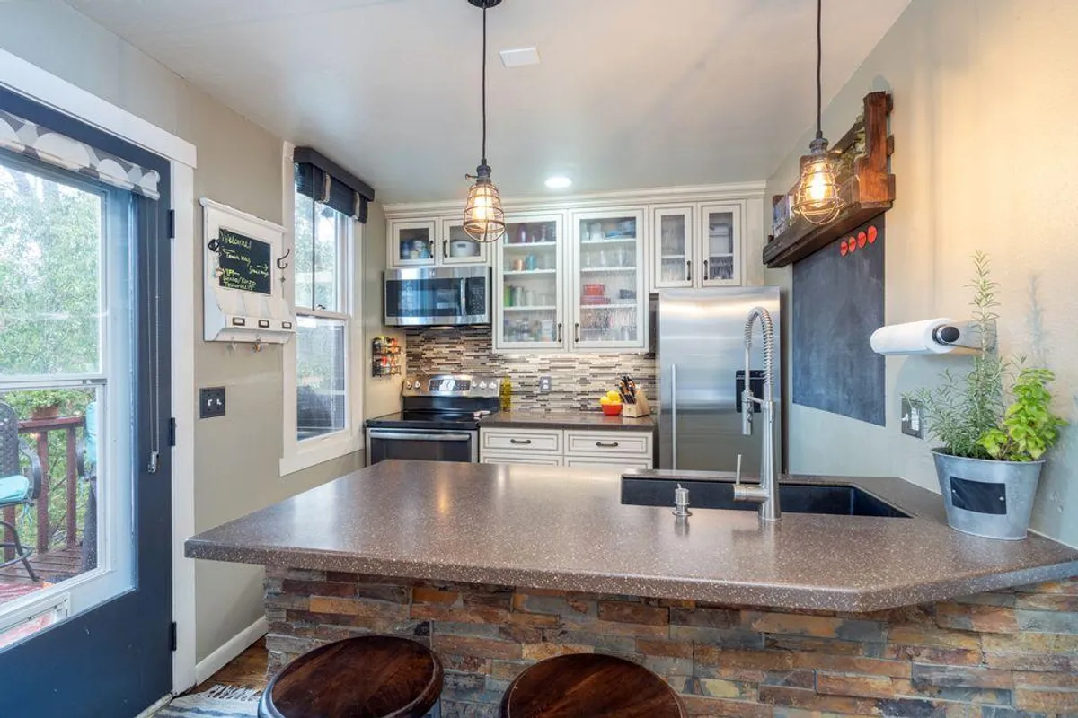 A bright kitchen with a central island, stainless steel appliances, and decorative touches. Windows bring in ample sunlight, making the space feel open and inviting for meal preparation or casual gatherings.
