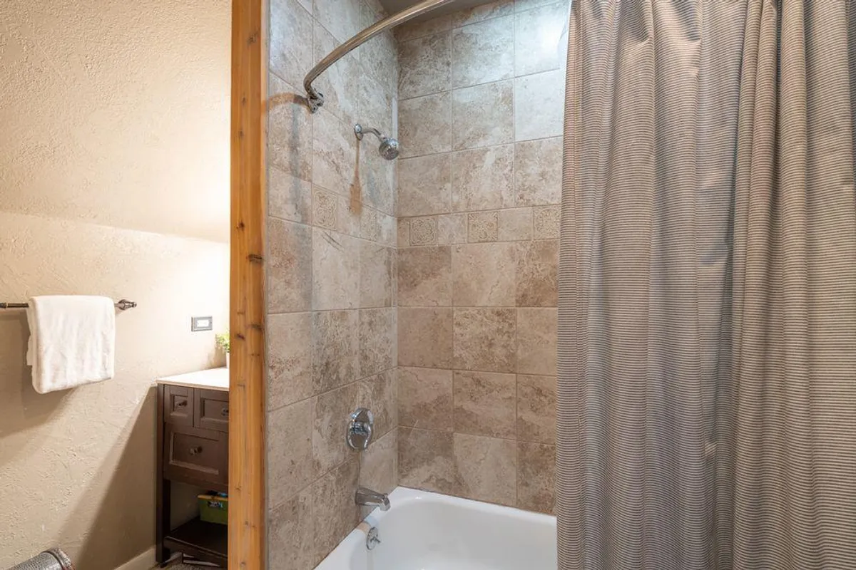A tranquil en suite bathroom featuring a deep shower/tub combo, a vanity with a large mirror, and a towel rack. The calming color palette and clean lines evoke a spa-like retreat, ideal for après-ski relaxation or bathtime with children.