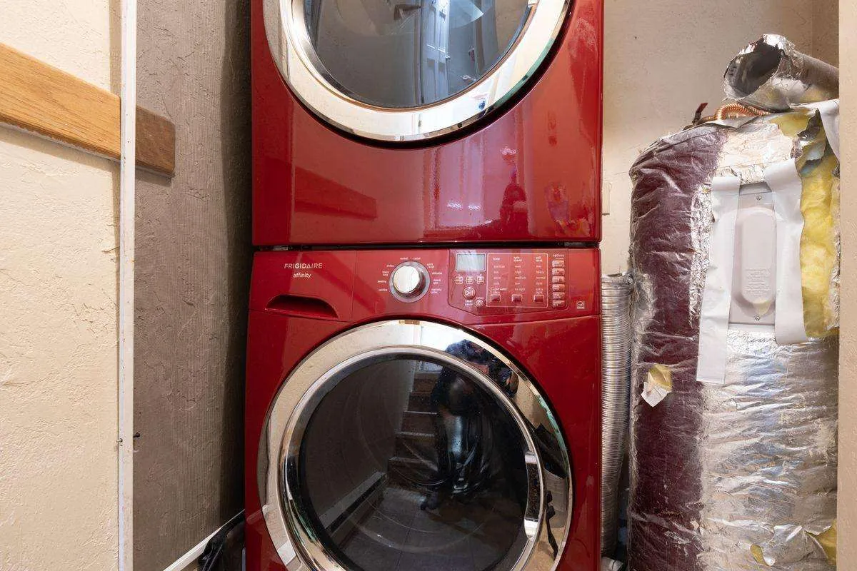 A neatly organized laundry area showing a stacked red washer and dryer next to a hot water tank and utility shelves. The space is clean and functional, catering to families and longer stays.